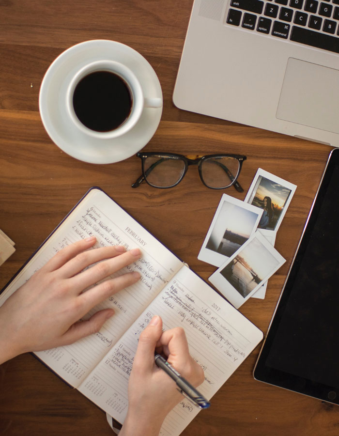 A person writing in a notebook near a computer